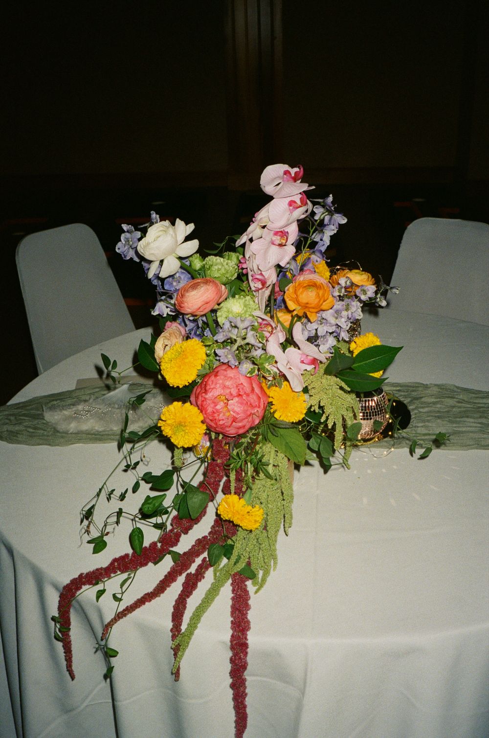 A vibrant floral centerpiece with pink, yellow, and orange blooms arranged on a white tablecloth at a formal event.
