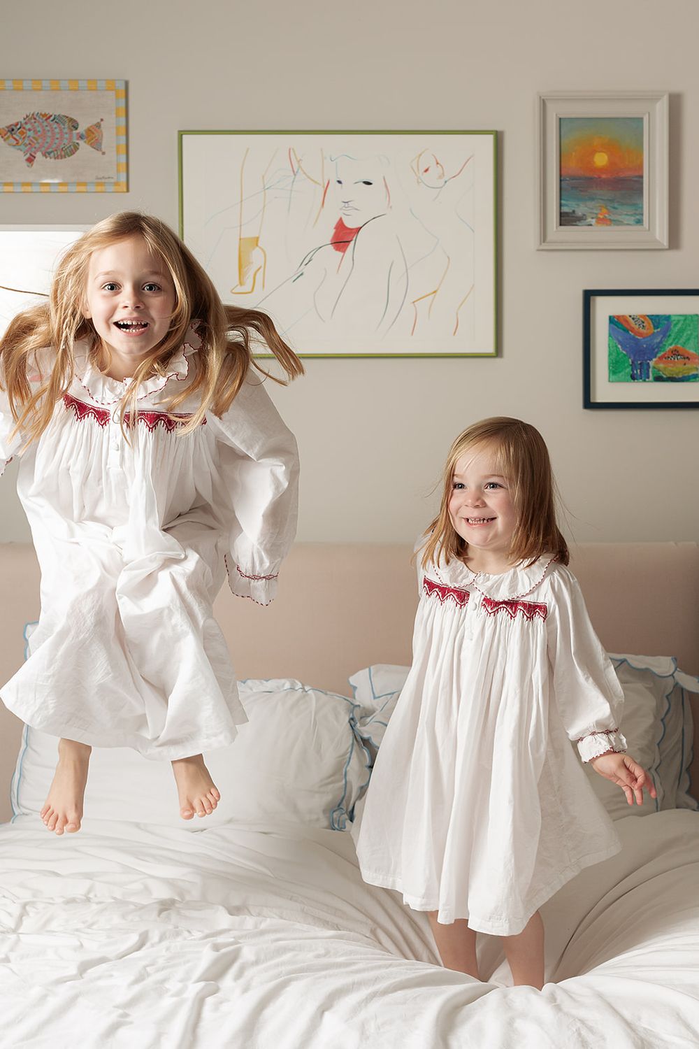In home, London, UK, family photography session. Sisters in matching Smock London night dresses jumping and playing on the bed.