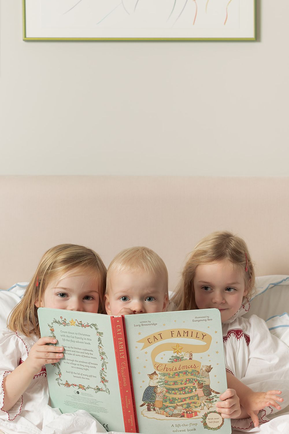 London family photo session, three sisters snuggled in bed reading children's book titled 'Cat Family Christmas' written by Lucy Brownridge.