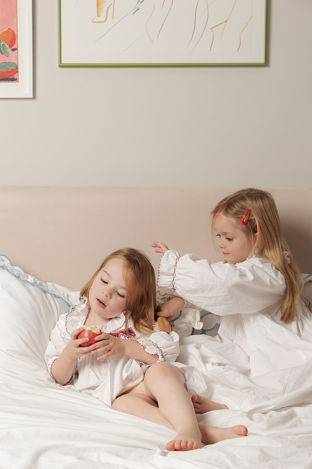 London, UK, family photography session. Sisters wearing matching Smock London night dresses, relaxing on the bed brushing their hair.