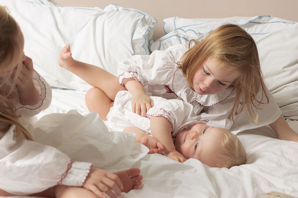 In home, London, UK, family photography session. Three sisters wearing matching Smock London night dresses, snuggling on the bed.