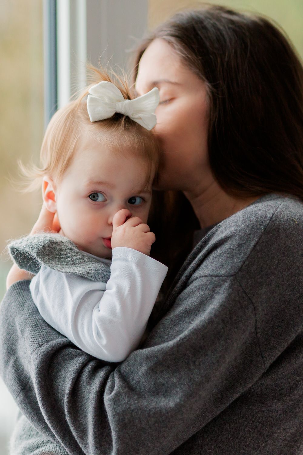 In home motherhood photography session. Loving kisses by the window with soft natural lighting.