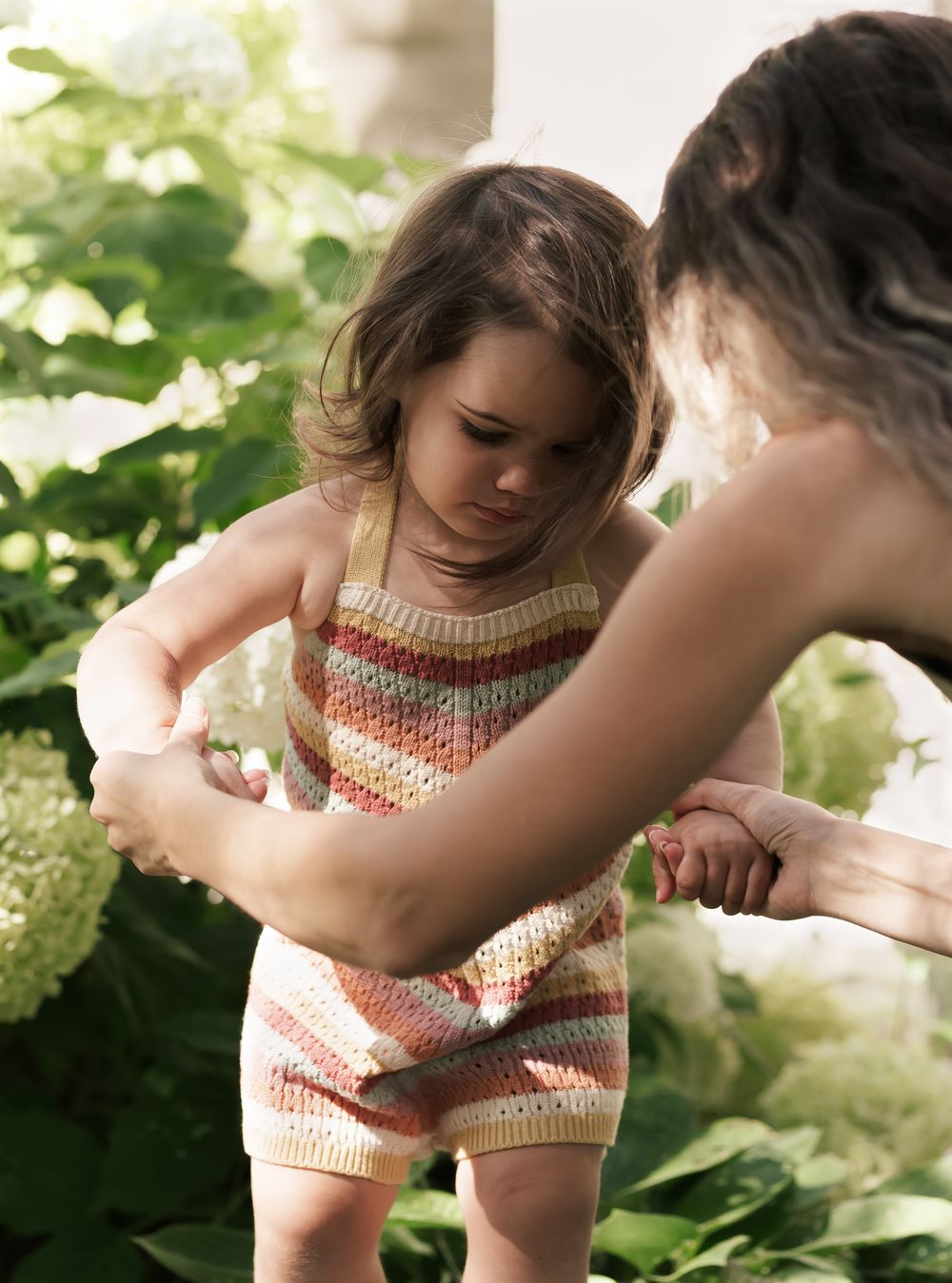 Motherhood outdoor photography session. Exploring outdoors among lush green hydrangea bushes in a summer garden.
