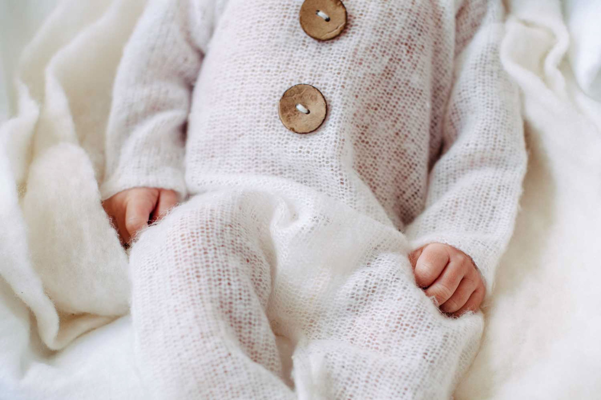 Close-up of knit baby outfit with brown wooden buttons on white fabric background.