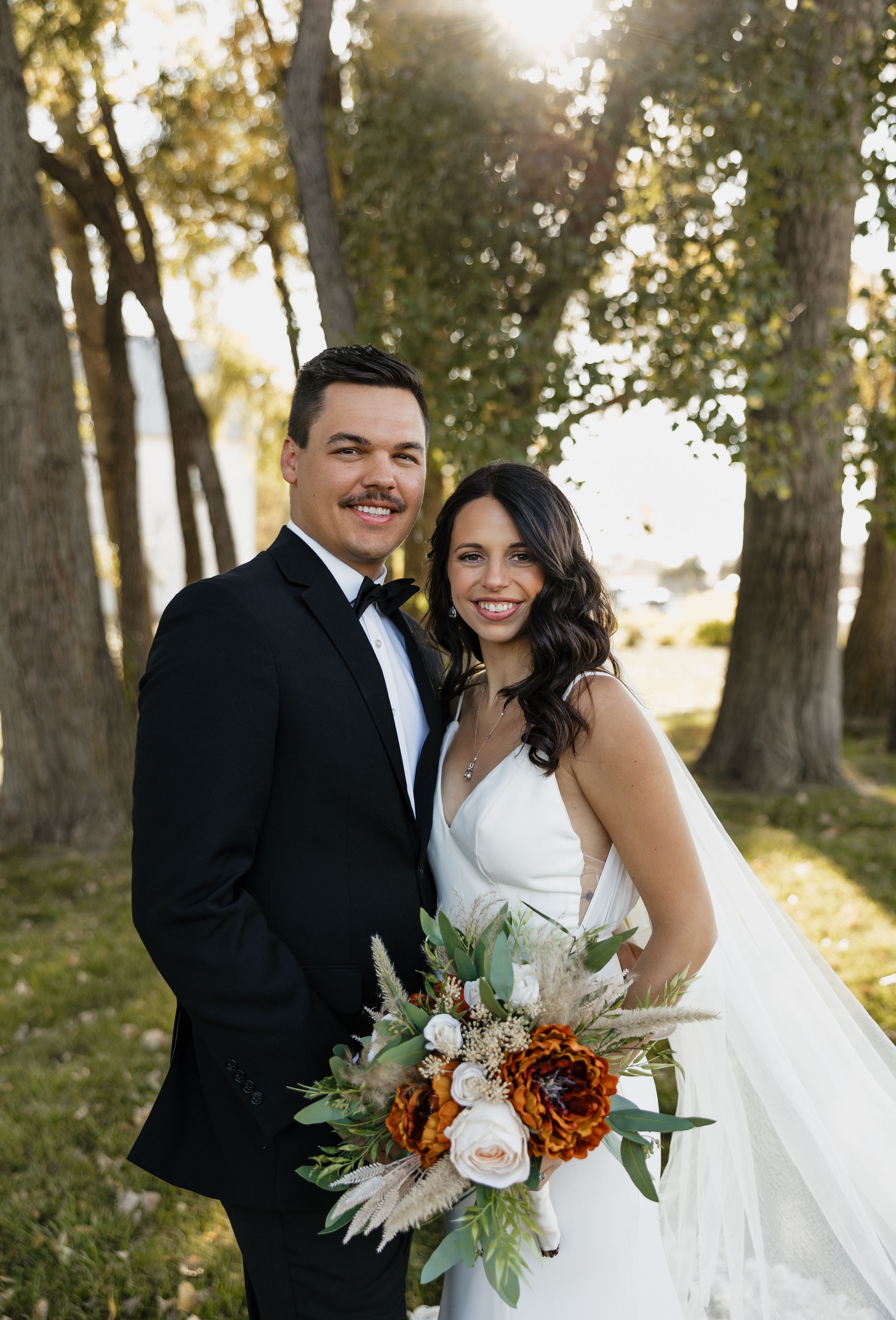 Wedding portrait with autumn-themed bouquet featuring orange flowers and greenery.