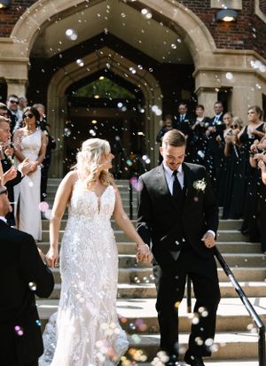 Wedding exit with bubbles as couple descends church steps in formal attire.