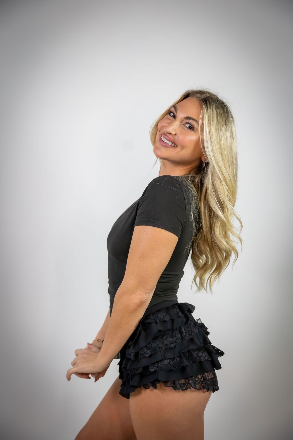 Playful studio portrait with black ruffled outfit against grey backdrop.