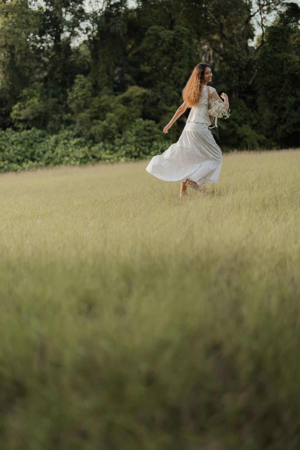 Person in flowing white dress twirls gracefully in a sunlit meadow.