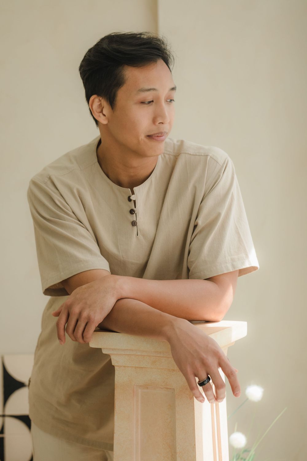Individual in beige shirt leans thoughtfully against light-colored pillar.