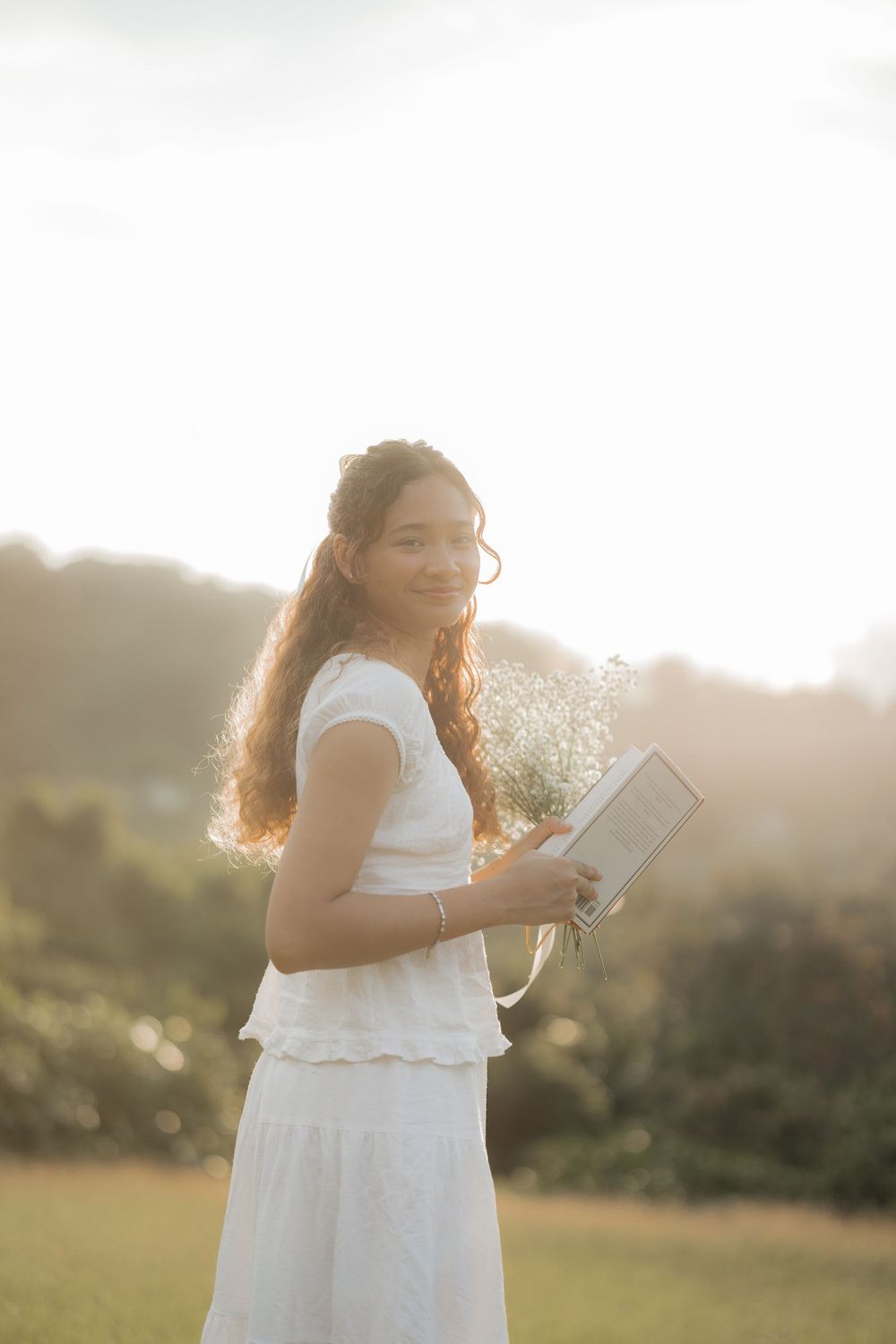 Candid moment captured of someone in white dress reading outdoors during golden hour.