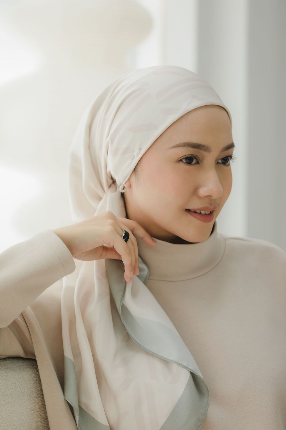 Person in white hijab and outfit poses elegantly against bright interior setting.