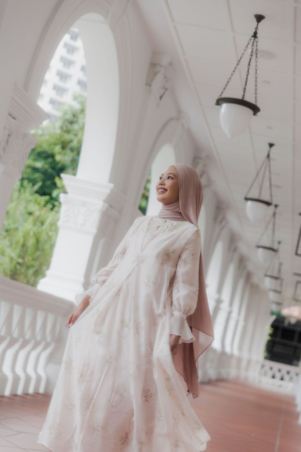 Person in flowing white dress twirls elegantly under white archways and hanging lamps.