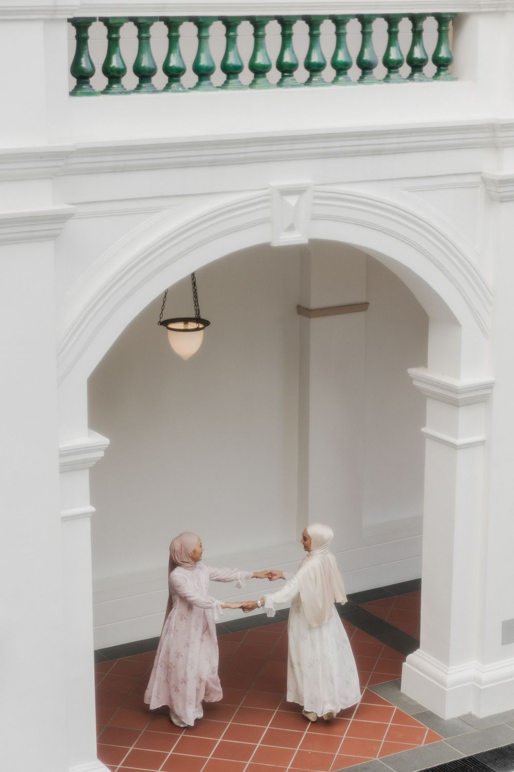 White colonial architecture with green balustrades frames two people in flowing dresses.