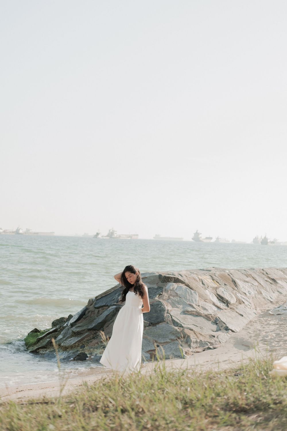White-dressed figure poses artistically near rocky coastal shoreline.