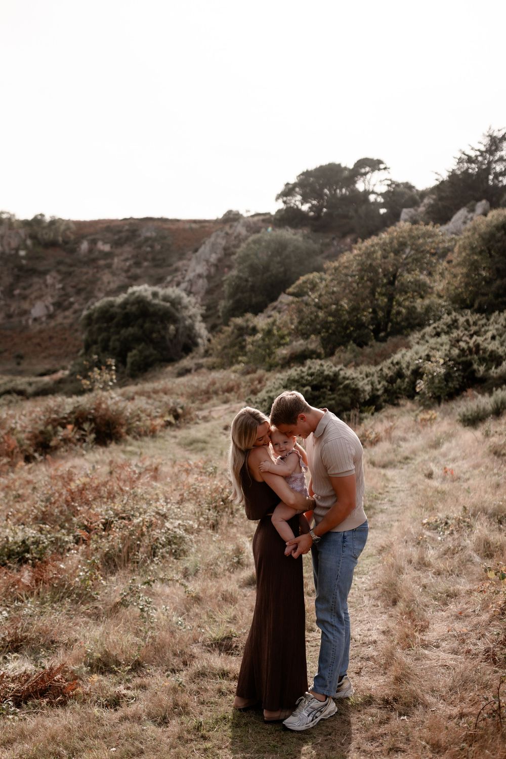 Family shares intimate moments together while sitting in tall grass on a hillside.