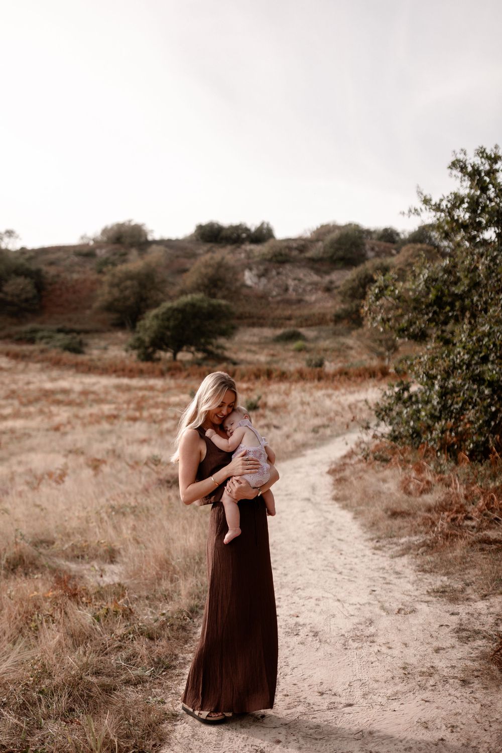 Family walking along dirt path surrounded by dry brush and hills.