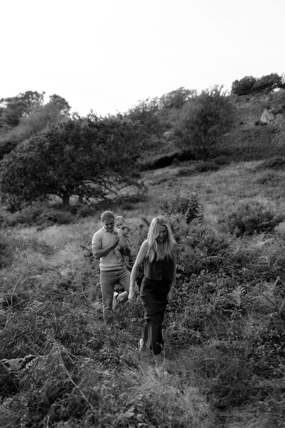 Black and white landscape photo shows family walking through brush on hillside.