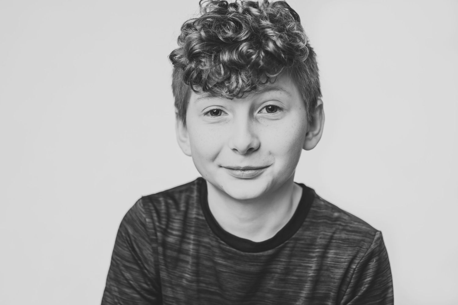 A black and white portrait of a young person wearing a striped shirt while smiling at the camera.