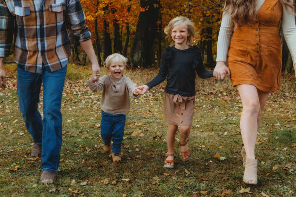 Casual family portrait with feet showing in autumn setting with fallen leaves.