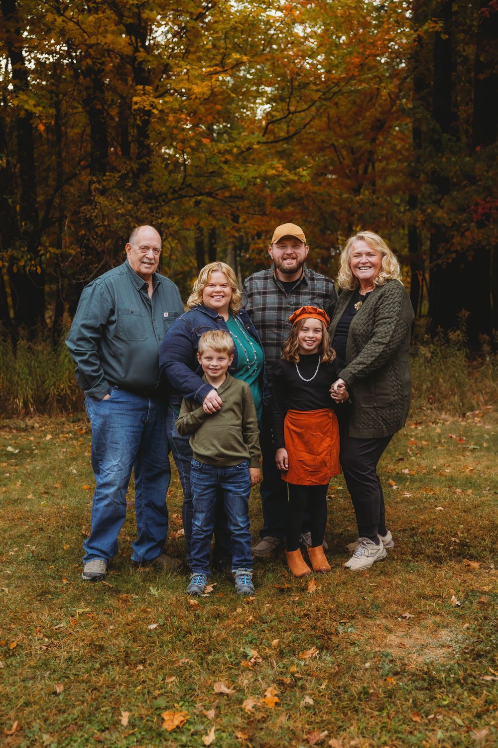A family group photo taken outdoors against a backdrop of vibrant autumn foliage.