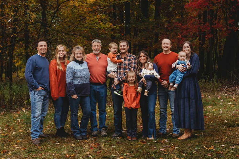 A group poses for autumn family portraits in a wooded area with colorful fall foliage in the background.