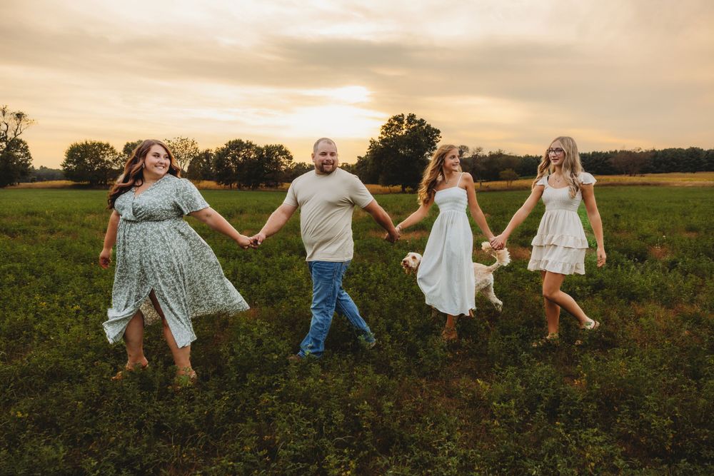A family holds hands while walking through a golden field at sunset.