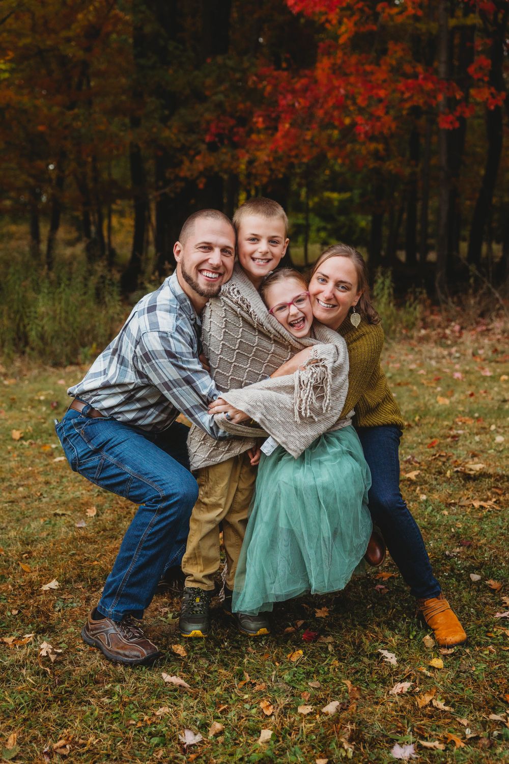A candid family moment captured with everyone laughing together on fallen autumn leaves.