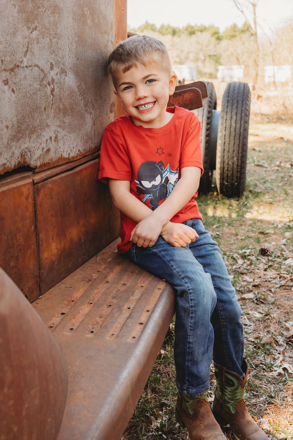 A young child in a red t-shirt sits on rustic metal bench outdoors.