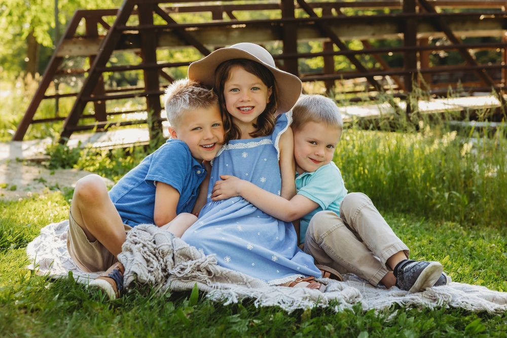 A family relaxes together on a picnic blanket in a sunny park setting.