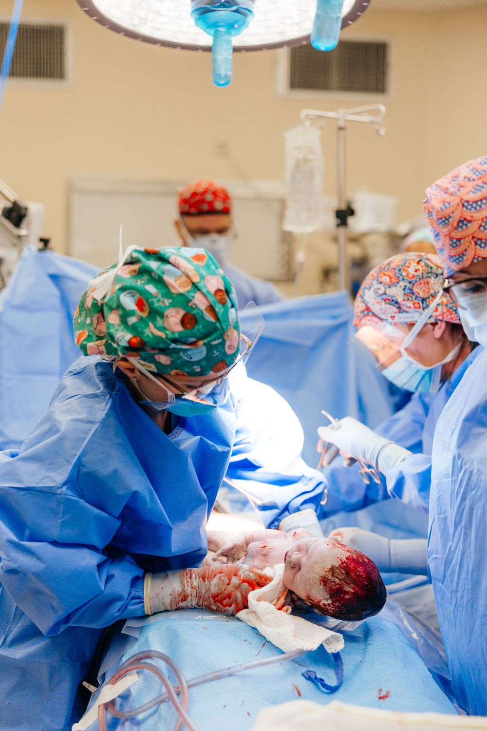 Medical team in blue scrubs and surgical caps perform an operation in a brightly lit operating room.