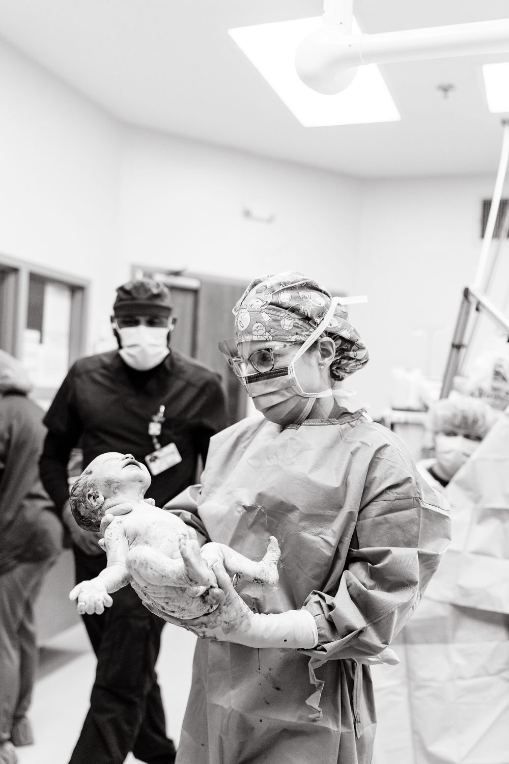 Medical professionals in surgical attire and masks work in a hospital operating room in black and white photography.