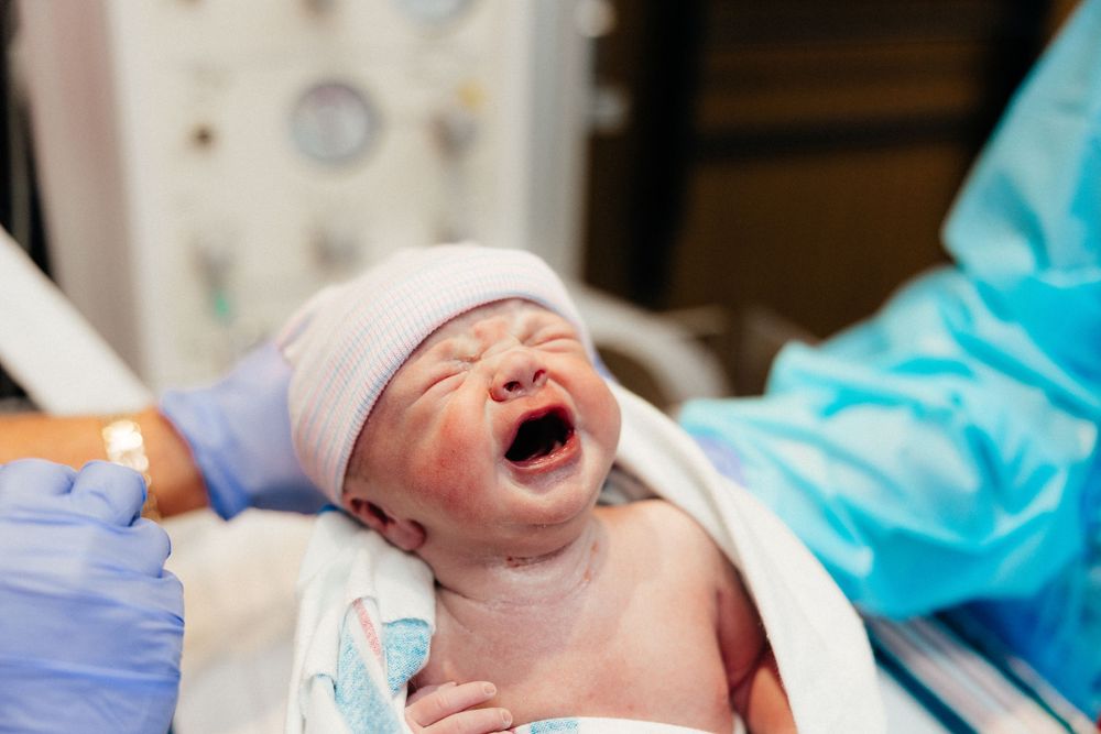 Newborn baby wearing white cap cries during first medical examination.