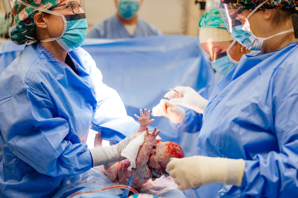 Medical team in blue scrubs and surgical masks performing a surgical procedure in an operating room.