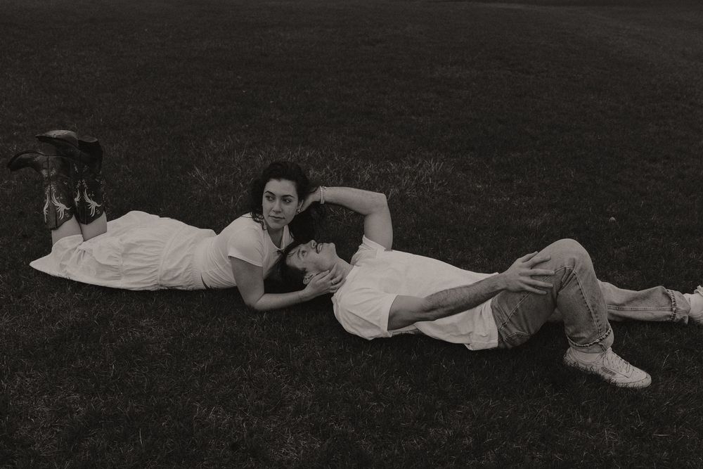 Vintage black and white photograph shows people lying down in a line on grass during an outdoor gathering.