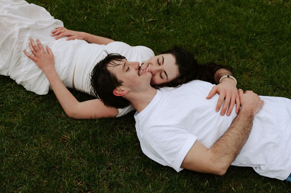 A person in a white shirt lies on green grass in a relaxed pose.