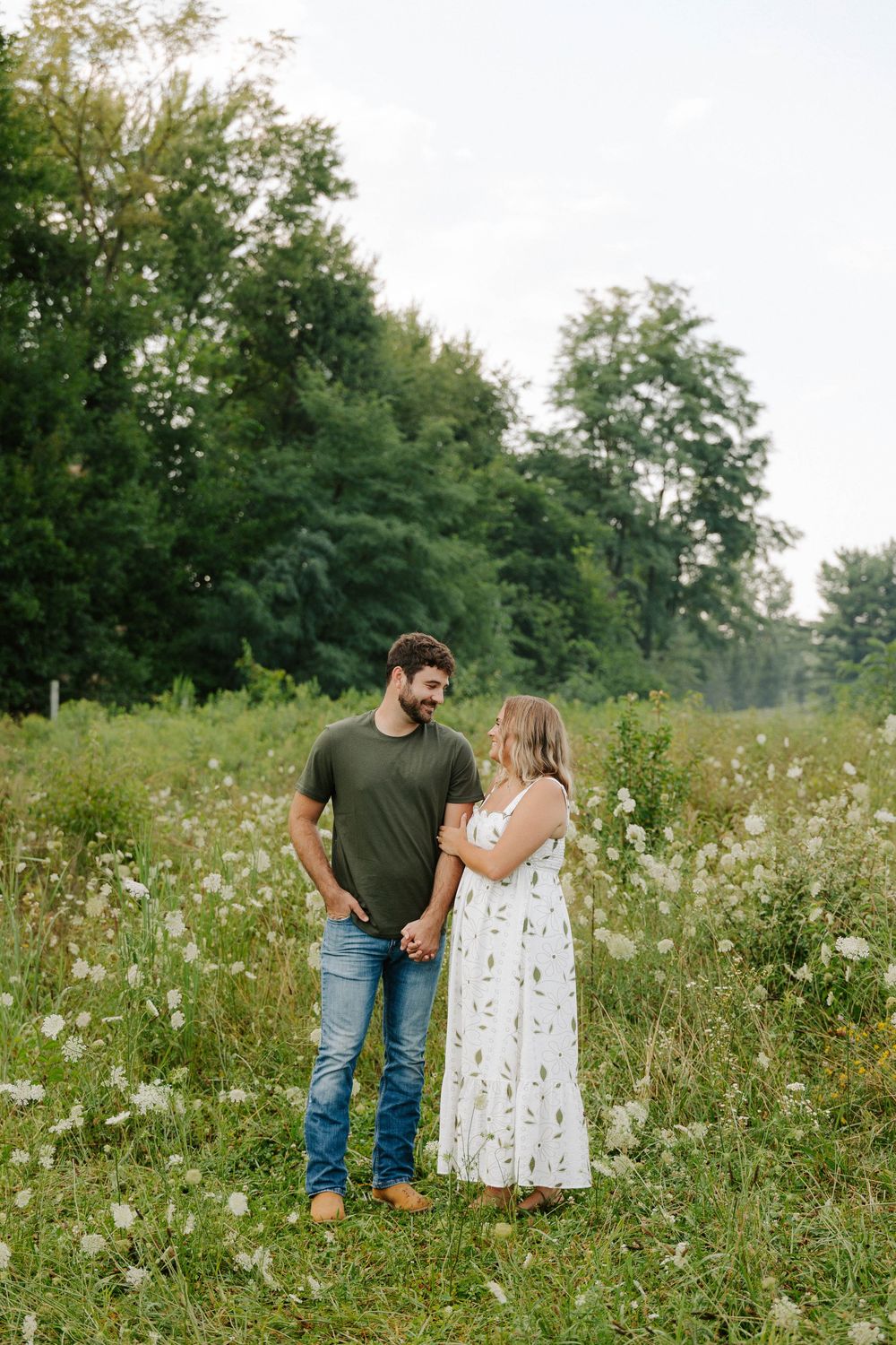 A couple shares a romantic moment in a wildflower meadow filled with white flowers and tall grass on a summer day.