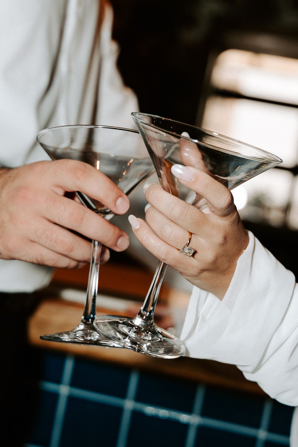 Close-up shot of hands holding martini glasses with a wedding ring visible.