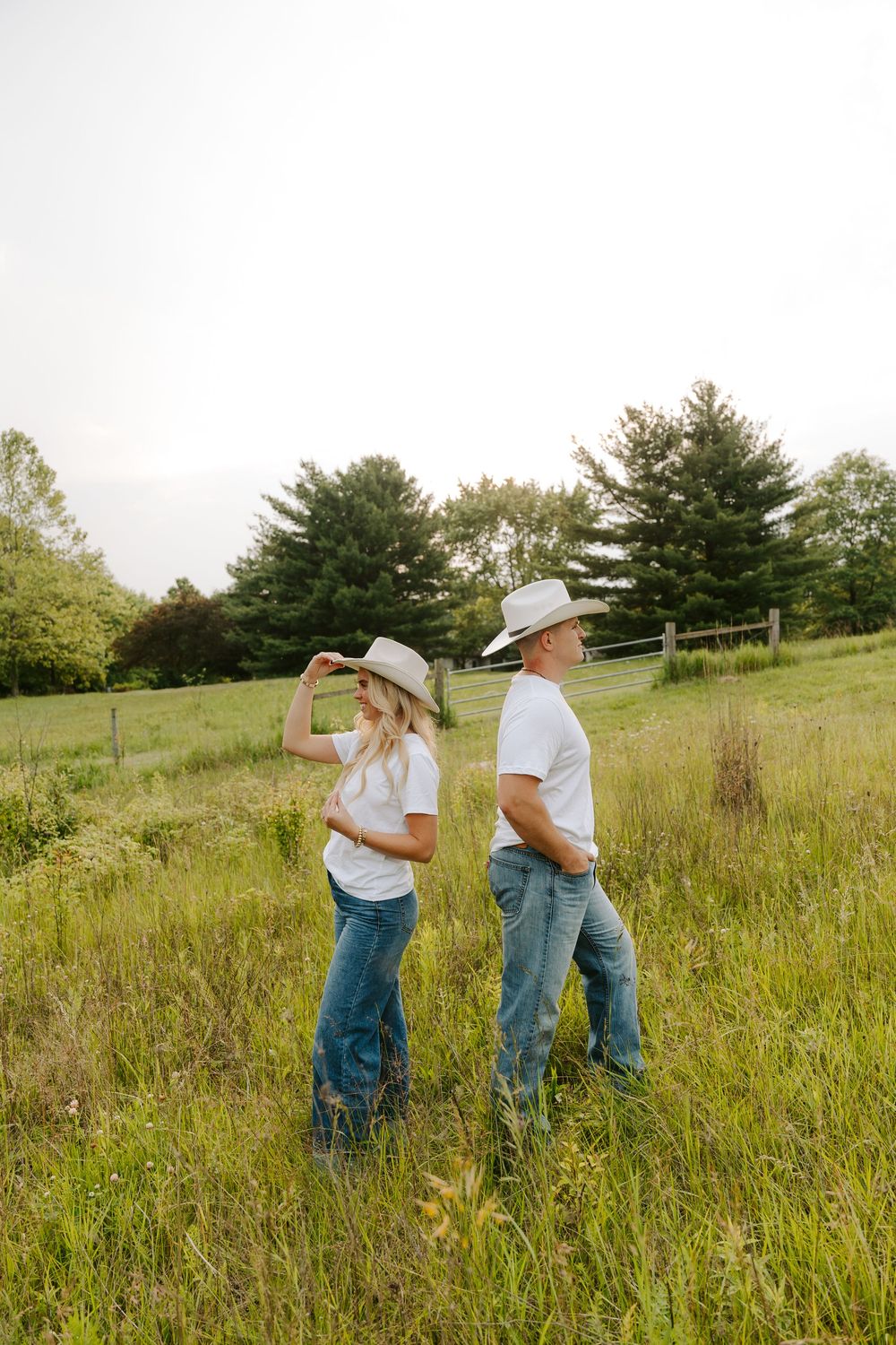 A romantic couple in cowboy hats and jeans share intimate moments in a sunlit meadow with tall grass.