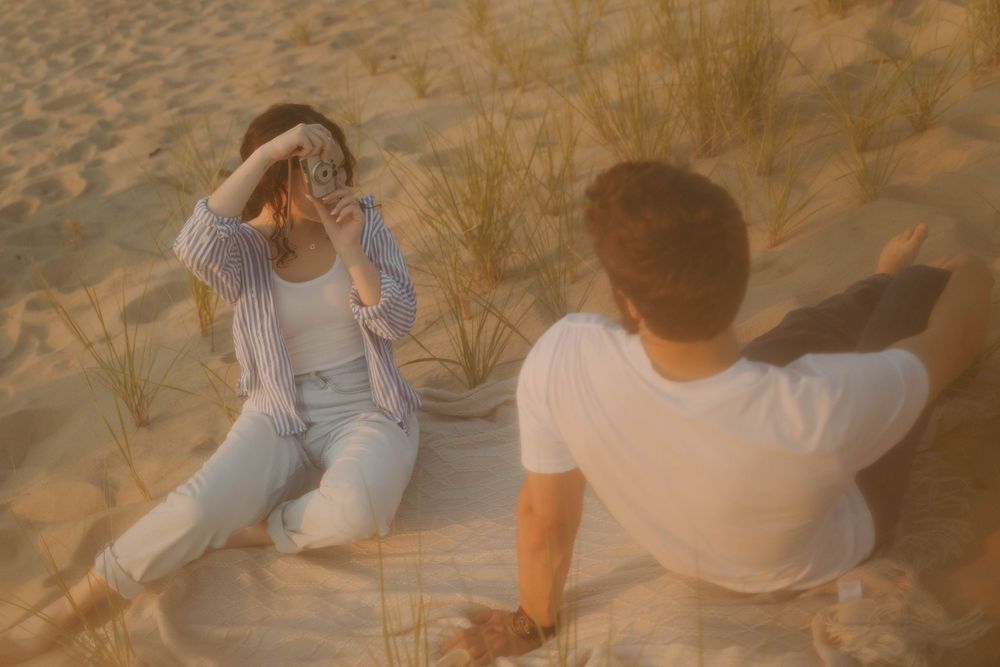 A person sitting in tall grass at sunset wearing casual clothes and taking in the peaceful natural scenery.