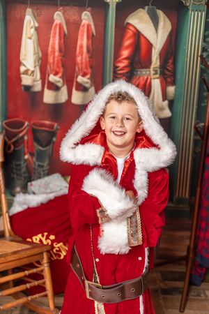 Red velvet Christmas display with Santa suits and boots hanging in a festive holiday backdrop.