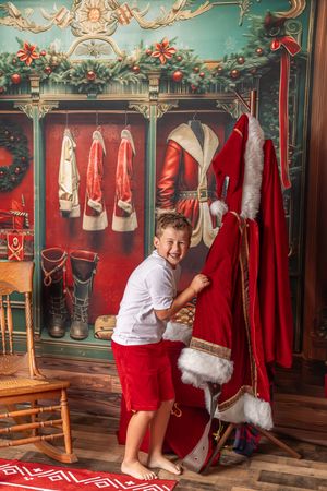 Festive holiday photo studio decorated with red Santa suits hanging on wall and Christmas greenery in turquoise room.