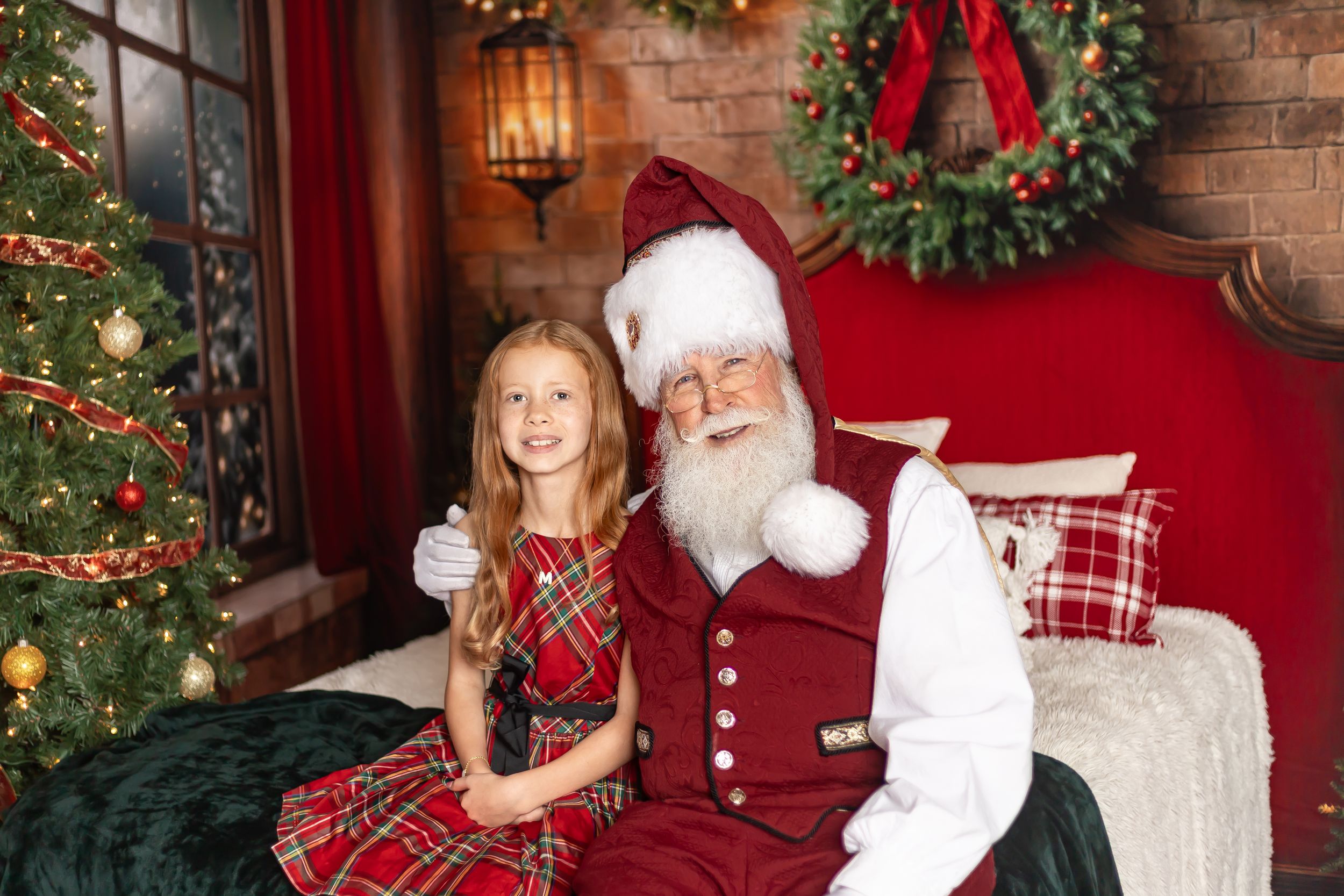 Santa wearing traditional red and white costume interacts with children by decorated holiday setting.