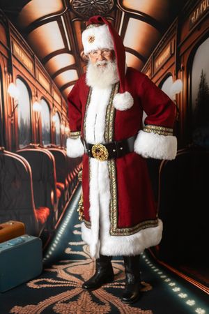Santa Claus in luxurious red and gold suit with white fur trim poses inside an elegant vintage train car.