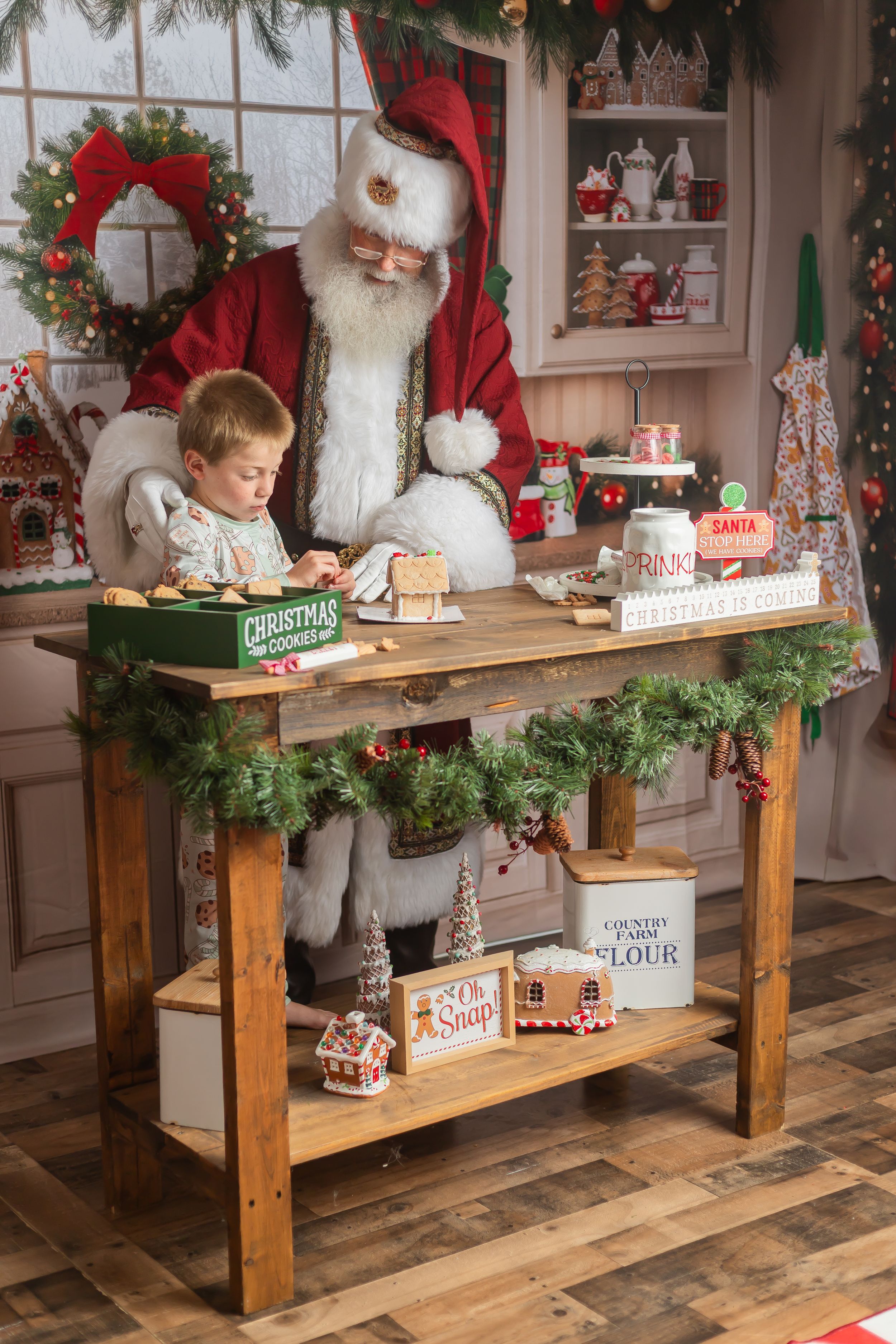 Young boy decorating Christmas cookies with Santa Claus at a festive wooden baking table with holiday decor.