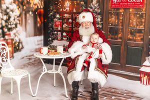 Santa Claus holds a baby in festive attire at a Christmas-themed photo set with cookies and holiday decorations.