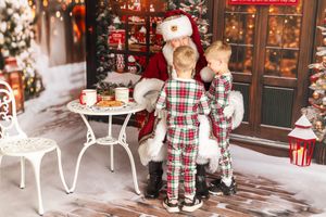 Two children in plaid pajamas visit Santa Claus beside a festive Christmas tree and holiday decorations.