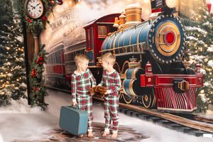 Two boys in matching plaid pajamas pose before a Polar Express Christmas train backdrop with festive decorations.