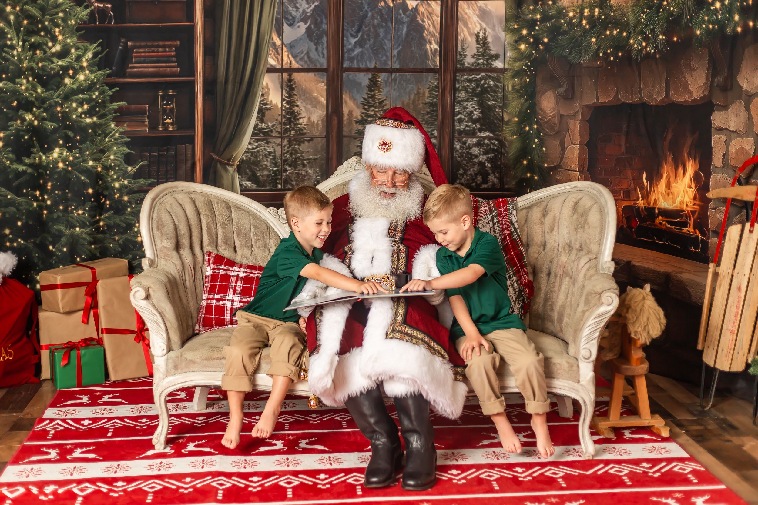 Santa reads a book with two young boys in green shirts on a festive chair by a decorated fireplace.