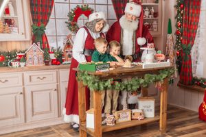Santa and Mrs. Claus help two children decorate Christmas cookies in a festive holiday kitchen.