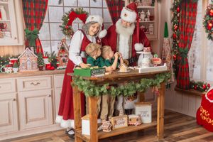 Santa and Mrs. Claus baking Christmas cookies with two young boys in a festive holiday kitchen.